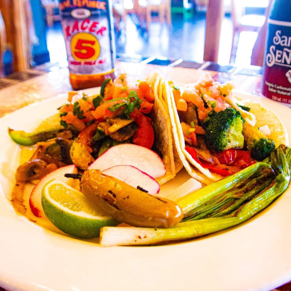 Two Los Cantaros Taqueria tacos filled with vegetables, served with lime, radishes, and grilled onions.