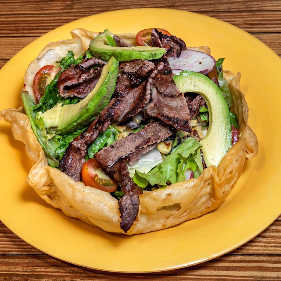 Los Cantaros Taqueria's taco salad with steak, avocado, lettuce, and tomatoes in a crispy tortilla bowl.