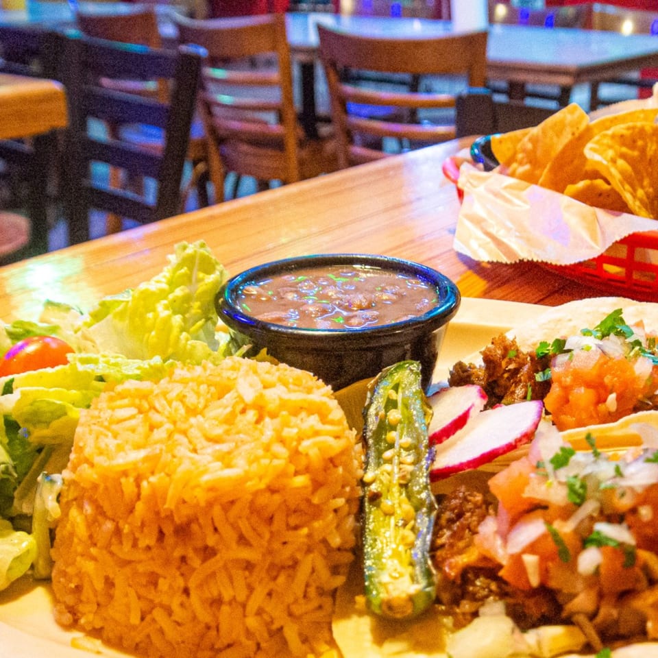 Mexican platter with tacos, rice, beans, salad, and a grilled jalapeño on a wooden table.