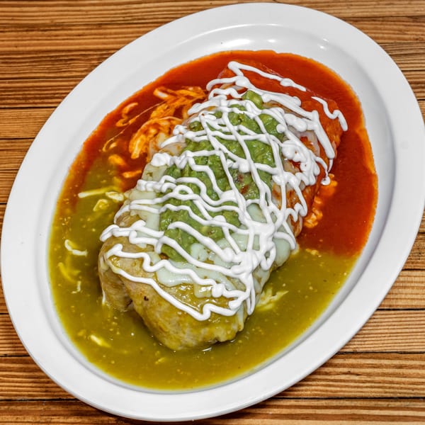 A Los Cantaros Taqueria burrito covered in red and green sauce, guacamole, and sour cream.